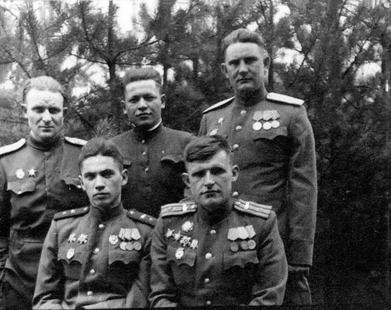 Black and white archival photo showing five Soviet Red Army officers in uniform with medals posing outdoors in a pine forest, April 1945.