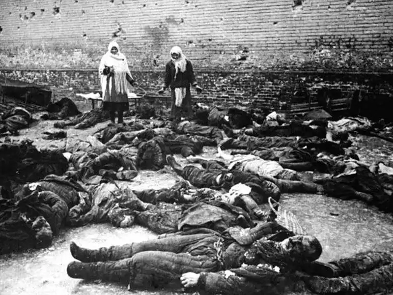 Black and white archival photograph of the prison yard in Rostov-on-Don with local civilians standing near brick wall in February 1943.
