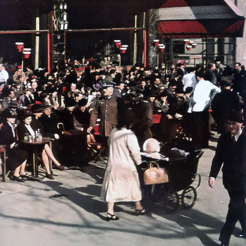 German Wehrmacht officers walking past a crowded café in occupied Paris, 1942 color photograph