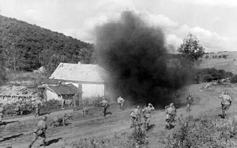 Soviet Red Army infantry charging past a cottage in Western Ukraine under heavy artillery shell detonation 1944.