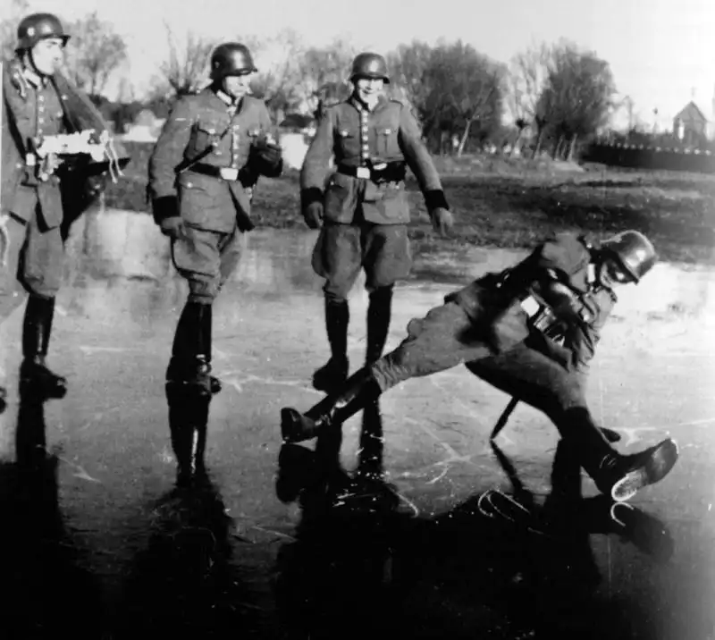 Four German police battalion soldiers walking on ice in the occupied USSR in 1942, with one soldier slipping and falling in a comical pose.