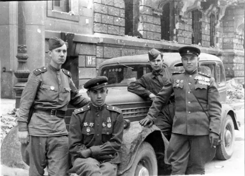 Black and white historical photo showing four Red Army officers posing next to a GAZ-11-73 staff sedan with painted military orders on the windshield in Berlin, May 9, 1945.