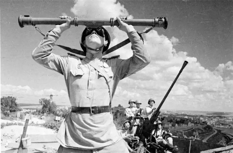A Soviet rangefinder sergeant looking through a long stereoscopic rangefinder with a 37mm 61-K anti-aircraft gun crew in the background overlooking Sevastopol in 1944.