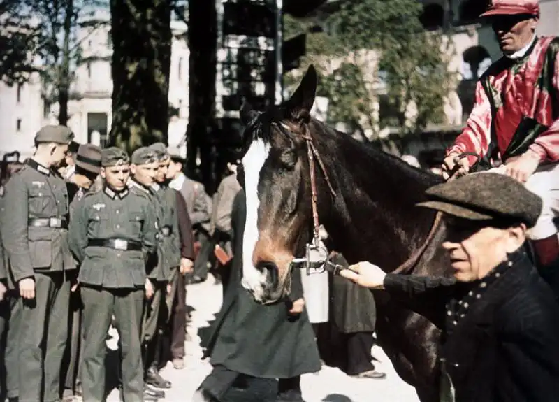Color WWII photograph of jockeys being weighed at Longchamp Racecourse in occupied Paris while German soldiers observe the event in 1943.