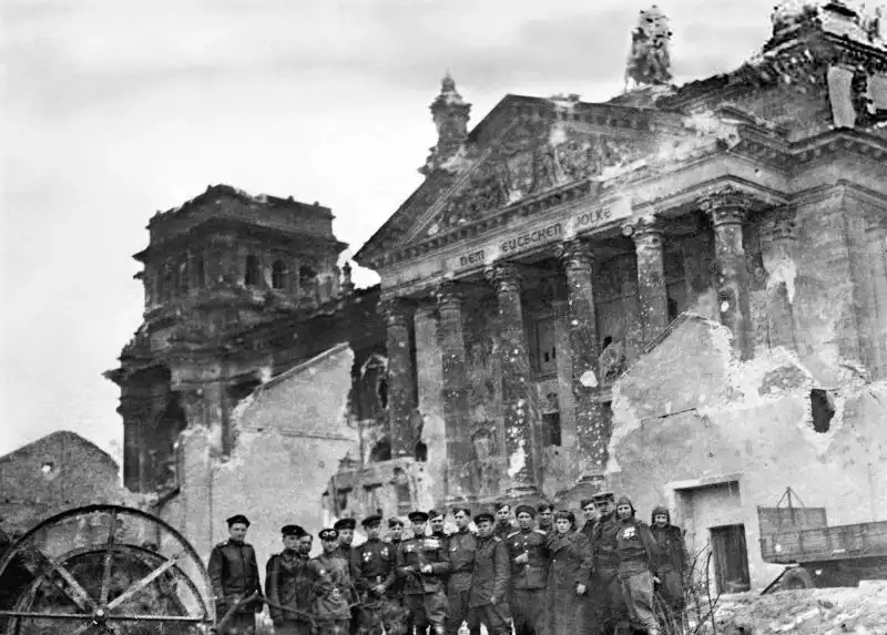 Black and white Victory Day photo showing a group of Soviet Red Army tank officers and soldiers posing in front of the damaged Reichstag building in Berlin, May 9, 1945.