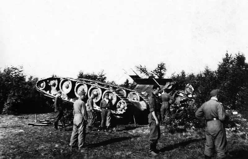 Black and white historical photo capturing German soldiers standing around an overturned Soviet T-34 tank with its tracks facing upward near Vilnius, June 1941.