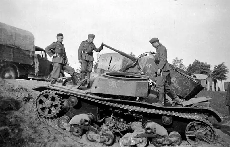 WWII photo of three German soldiers inspecting a destroyed Soviet T-26 light tank with conical turret, roadside, USSR, summer 1941.