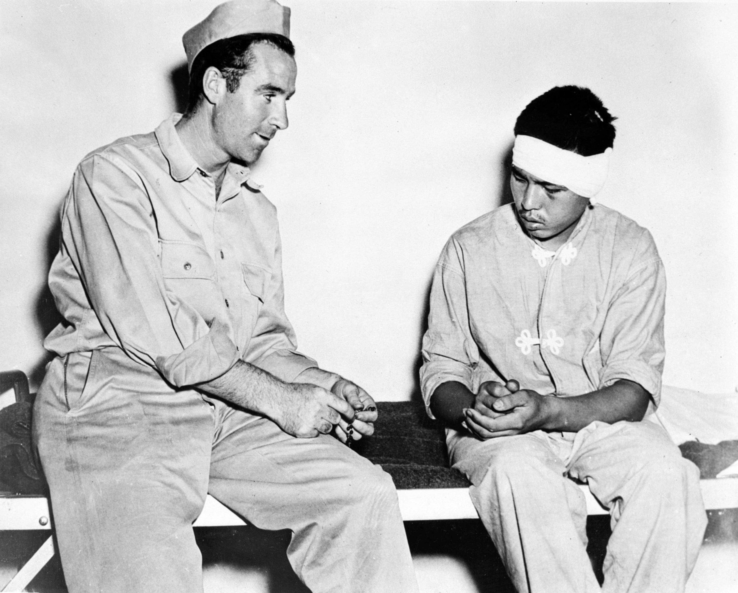 US Private Henry F. Rourke speaks to a wounded Japanese POW